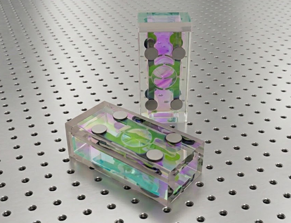 Two glass prisms with optical coatings and metal contact points for quantum experimentation are positioned for display on an optical breadboard